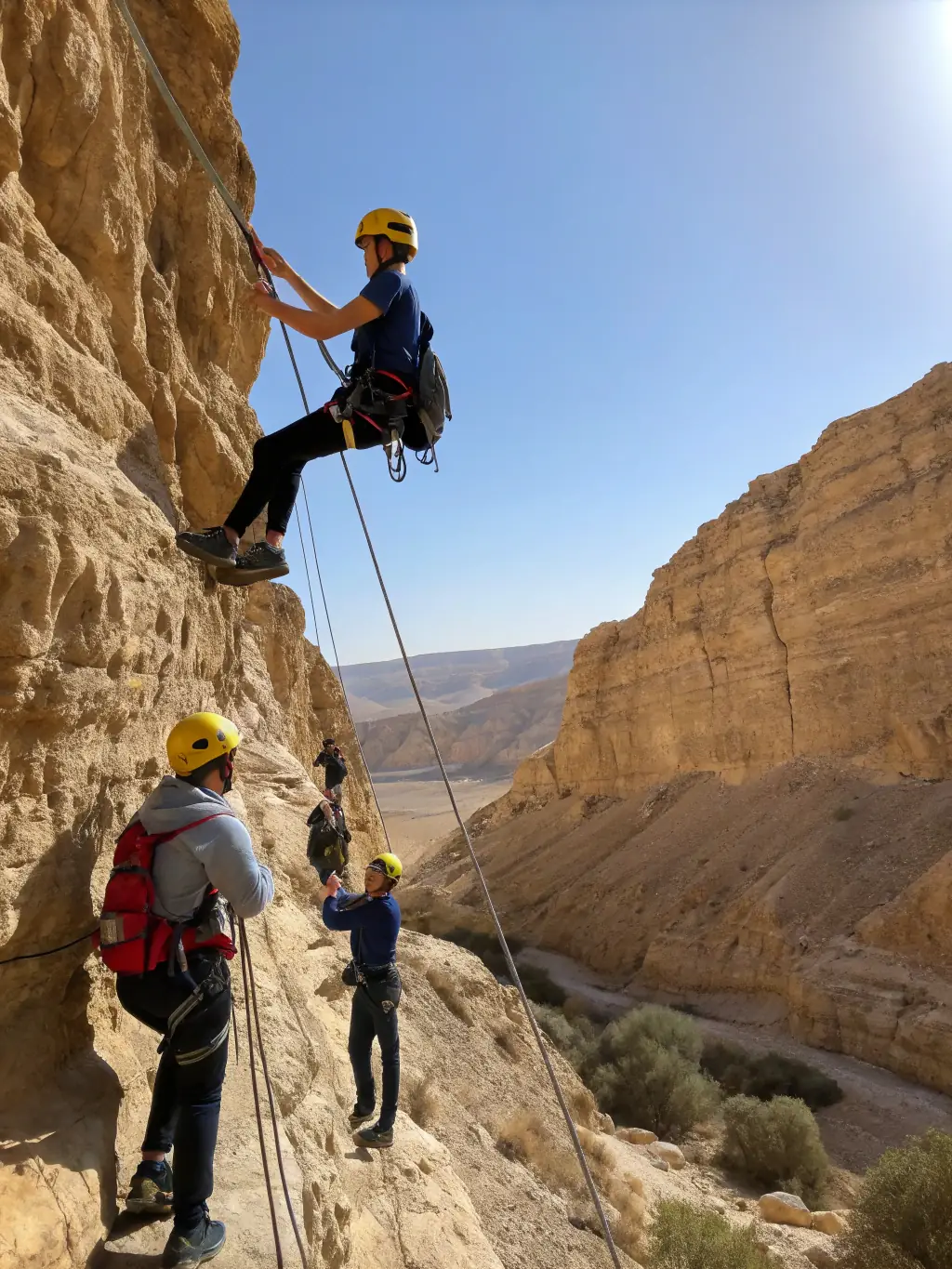 Teenagers rappelling down a rock face in the Judean desert, guided by experienced instructors.